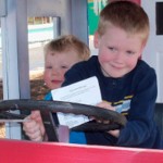 Two young boys behind wheel of a play train.